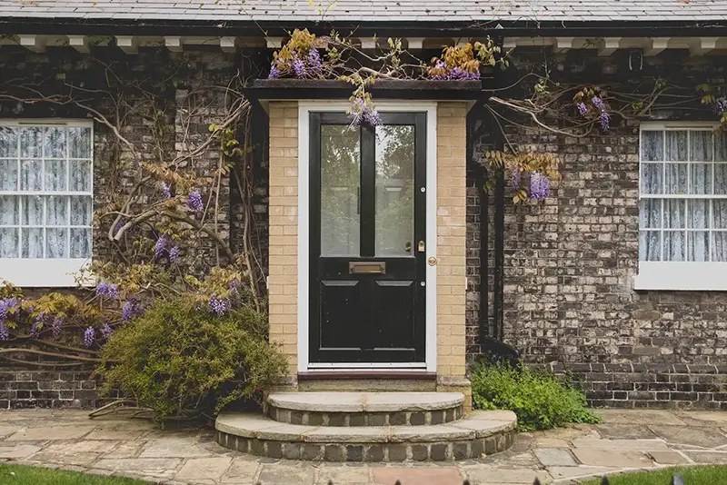 a photograph of a classic, earthy-colored brick home covered in vines with a front door that has a glass insert