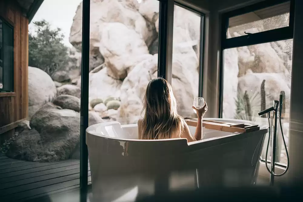 A woman sitting in a large bathtub in a well-designed bathroom with glass windows